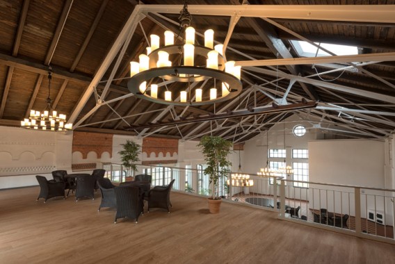 Ein geräumiges Loft mit freiliegenden Holzbalken, großen Fenstern, Korbmöbeln, Topfpflanzen und mehreren runden Kronleuchtern, die von der Decke hängen.