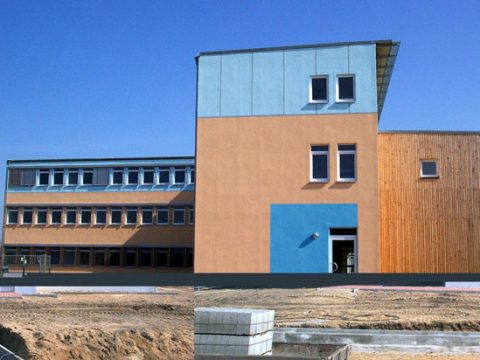 Ein modernes, rechteckiges Gebäude mit blauer, beiger und hölzerner Fassade, mit mehreren Fenstern und einem geometrischen, turmähnlichen Abschnitt, vor einem klaren blauen Himmel.