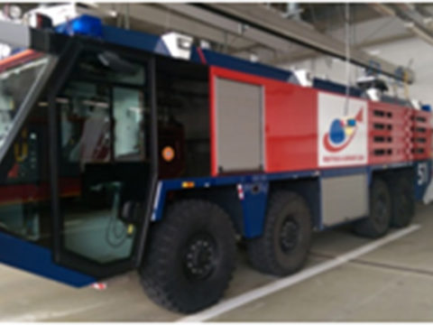 Großes Flughafen-Feuerwehrfahrzeug mit sechs Rädern, roter und blauer Karosserie und Notfallausrüstung, das in einer Garage der Feuerwache abgestellt ist.