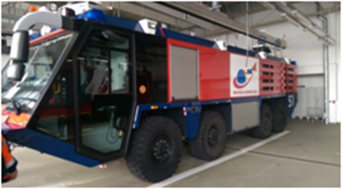 Großes Flughafen-Feuerwehrfahrzeug mit sechs Rädern, roter und blauer Karosserie und Notfallausrüstung, das in einer Garage der Feuerwache abgestellt ist.
