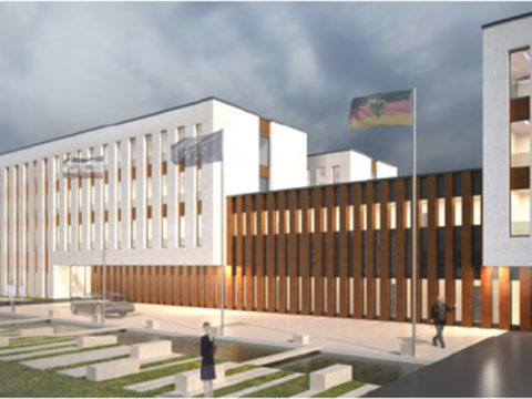 Modernes dreistöckiges Gebäude mit hohen Fenstern; die Menschen gehen bei bewölktem Himmel in der Nähe von Fahnenmasten und einer Grünanlage spazieren.