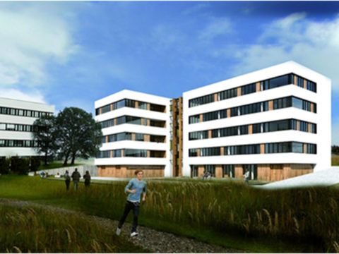 Ein modernes, weißes, mehrstöckiges Gebäude mit großen Fenstern steht in der Nähe einer Grünfläche mit Menschen, die unter einem teilweise bewölkten Himmel spazieren gehen und joggen.