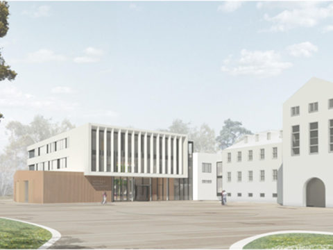 Ein modernes, weißes, mehrstöckiges Gebäude mit vertikalen Fensterlamellen steht neben älteren, weißen Gebäuden auf einem offenen, weitläufigen Platz, auf dem nur wenige Menschen unterwegs sind.