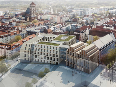 Luftaufnahme eines modernen, mehrstöckigen Gebäudekomplexes mit begrünten Dächern inmitten älterer, rot gedeckter Gebäude in einer europäischen Stadt.