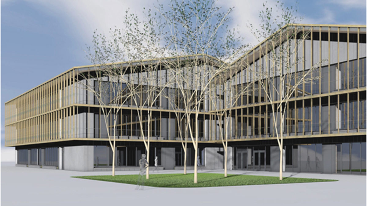 Modernes dreistöckiges Gebäude mit Glas- und Holzpaneelfassade, das einen Innenhof mit mehreren blattlosen Bäumen und grünem Gras unter einem teilweise bewölkten Himmel aufweist.