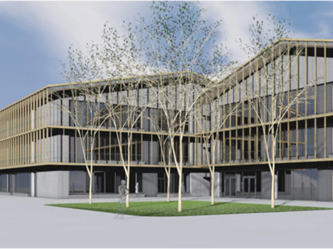 Modernes dreistöckiges Gebäude mit Glas- und Holzpaneelfassade, das einen Innenhof mit mehreren blattlosen Bäumen und grünem Gras unter einem teilweise bewölkten Himmel aufweist.