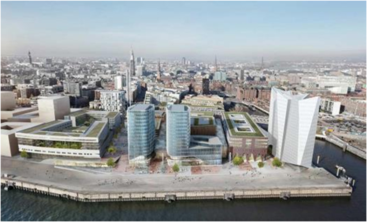Luftaufnahme einer modernen Stadtlandschaft am Wasser mit drei Glasgebäuden, einer weißen, kantigen Struktur und angrenzenden Straßen mit umliegender Bebauung.