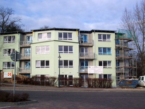 Ein im Bau befindliches dreistöckiges Wohnhaus mit Gerüsten an einer Seite, Baumaterialien, einem Container und einem davor geparkten Lastwagen.